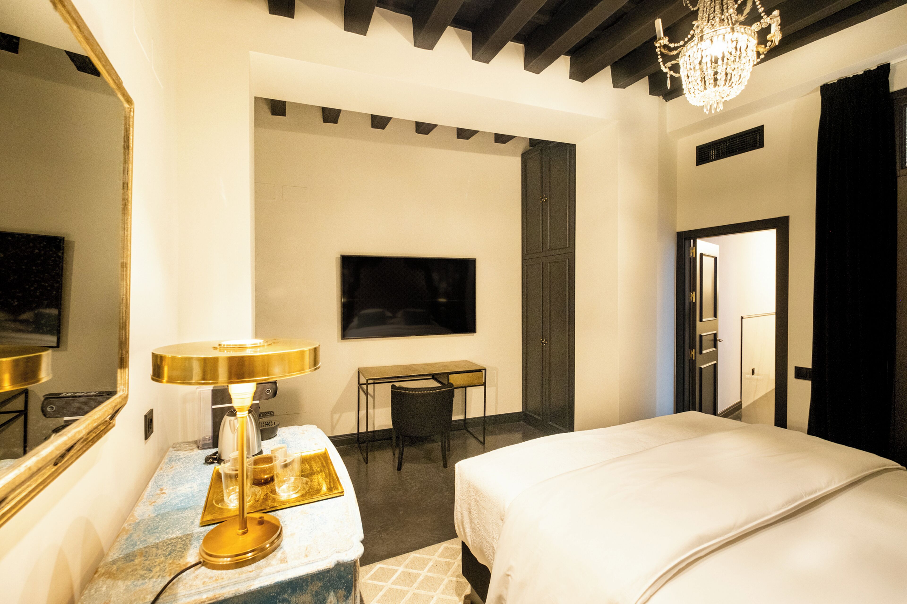Una habitación de hotel con cama, escritorio, silla, televisor y candelabro.