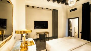 Una habitación de hotel con cama, escritorio, silla, televisor y candelabro.