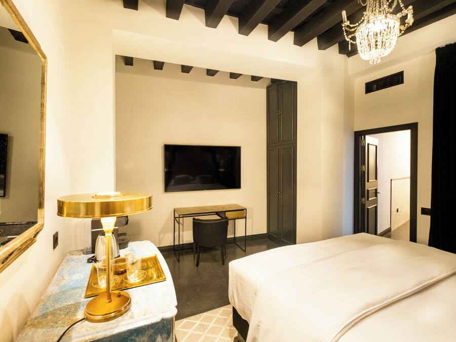 Una habitación de hotel con cama, escritorio, silla, televisor y candelabro.