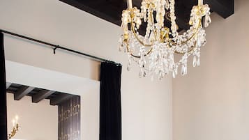 A modern hotel room with a chandelier, a black sofa with cushions, a coffee table with a tray, and a bed with white linens.