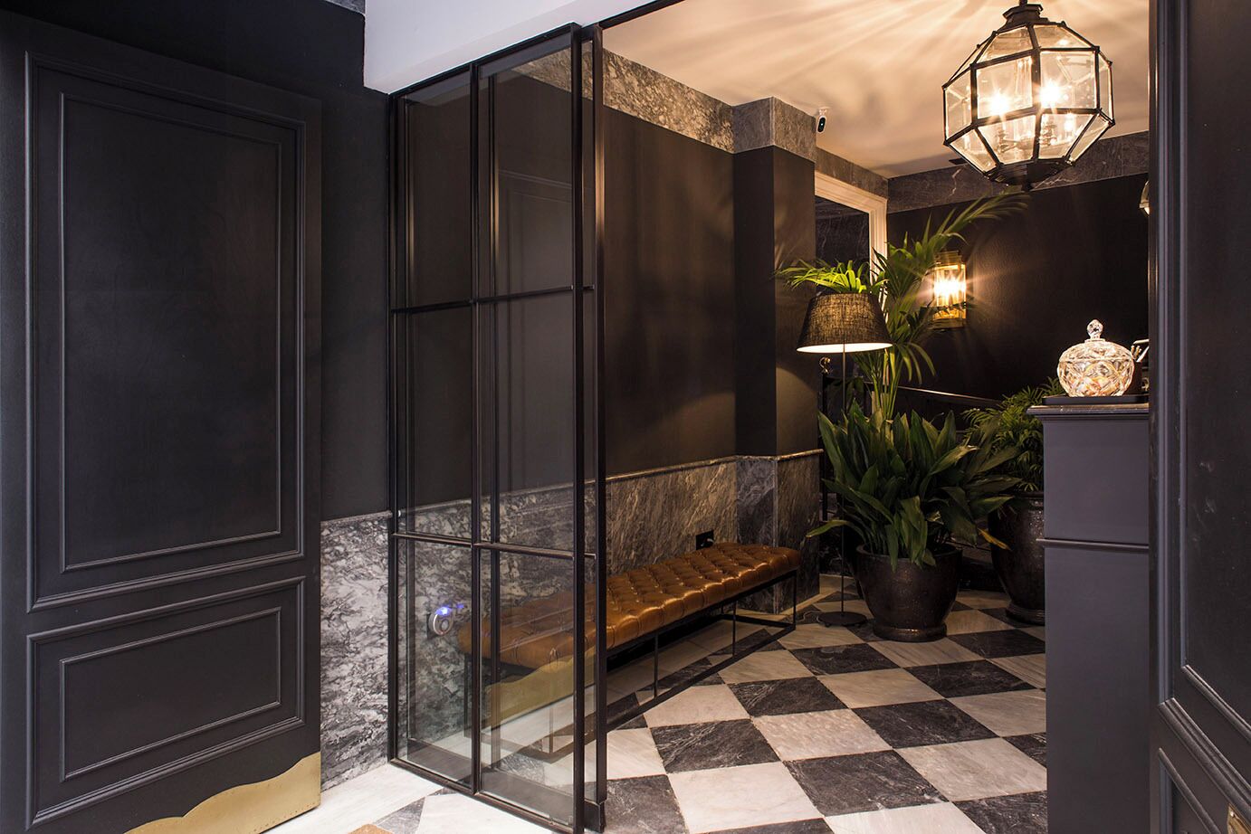 Een modern interieur met een zwart-wit geruit vloertje, een glazen scheidingswand, een bank en een hanglamp.