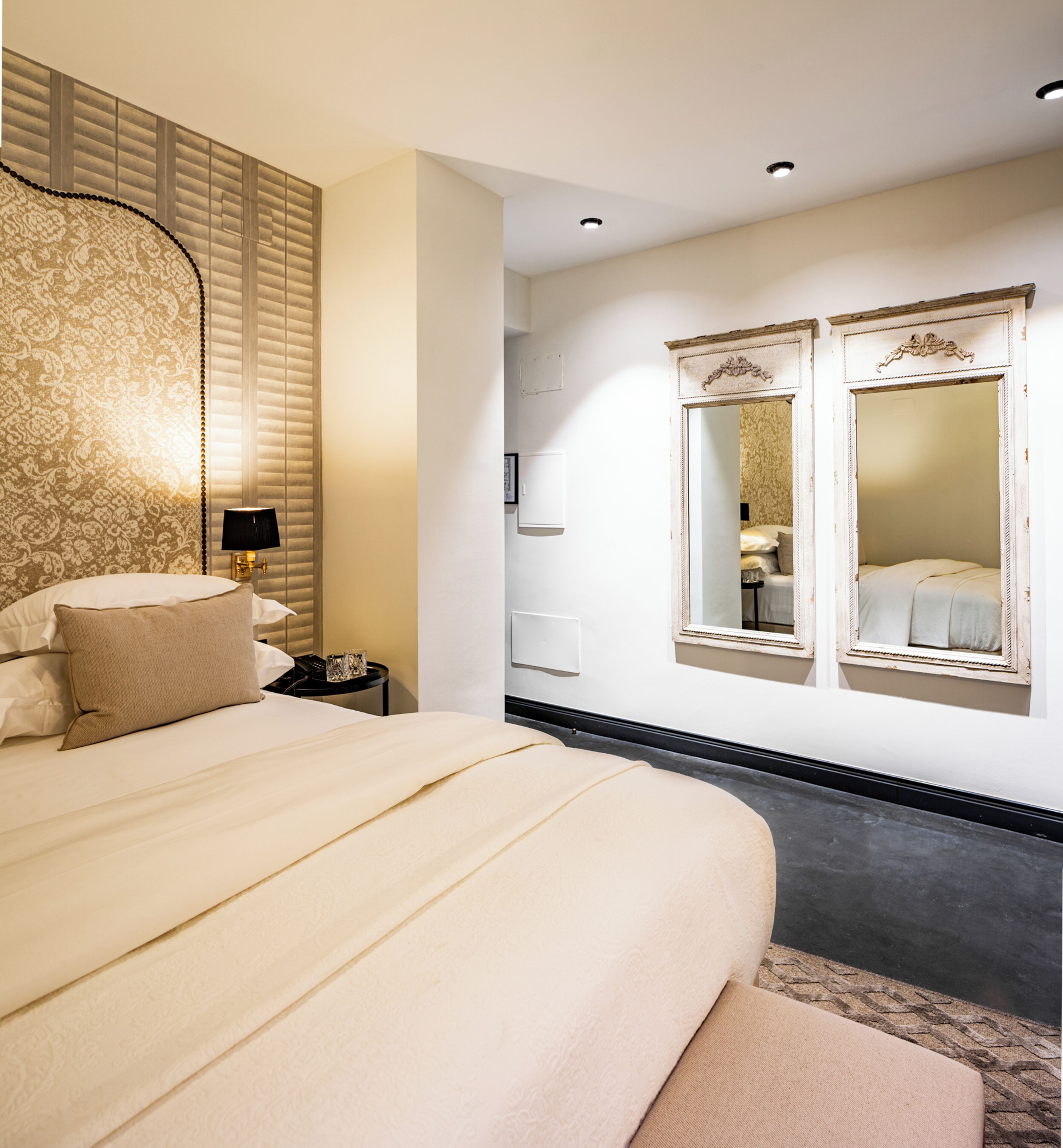 Una habitación de hotel con una cama grande, una mesita de noche con lámpara y dos espejos en la pared.