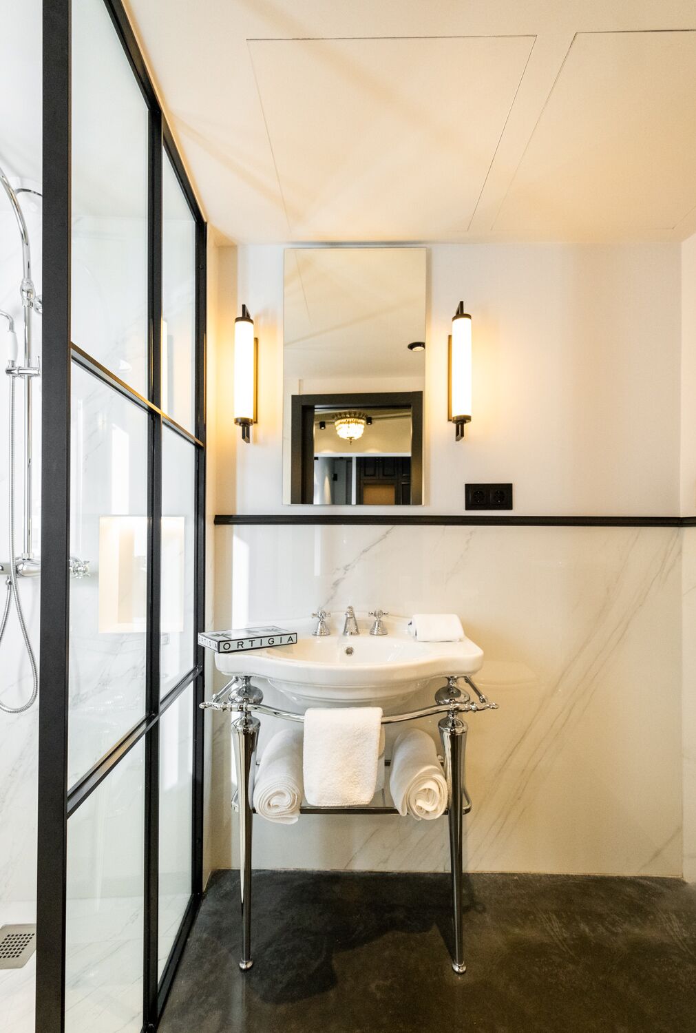 A modern bathroom with a marble sink, two wall-mounted lights, a glass shower enclosure, and a mirror above the sink.