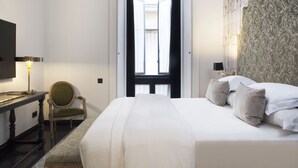 A hotel room with a large bed, a desk with a lamp, a chair, and a chandelier.