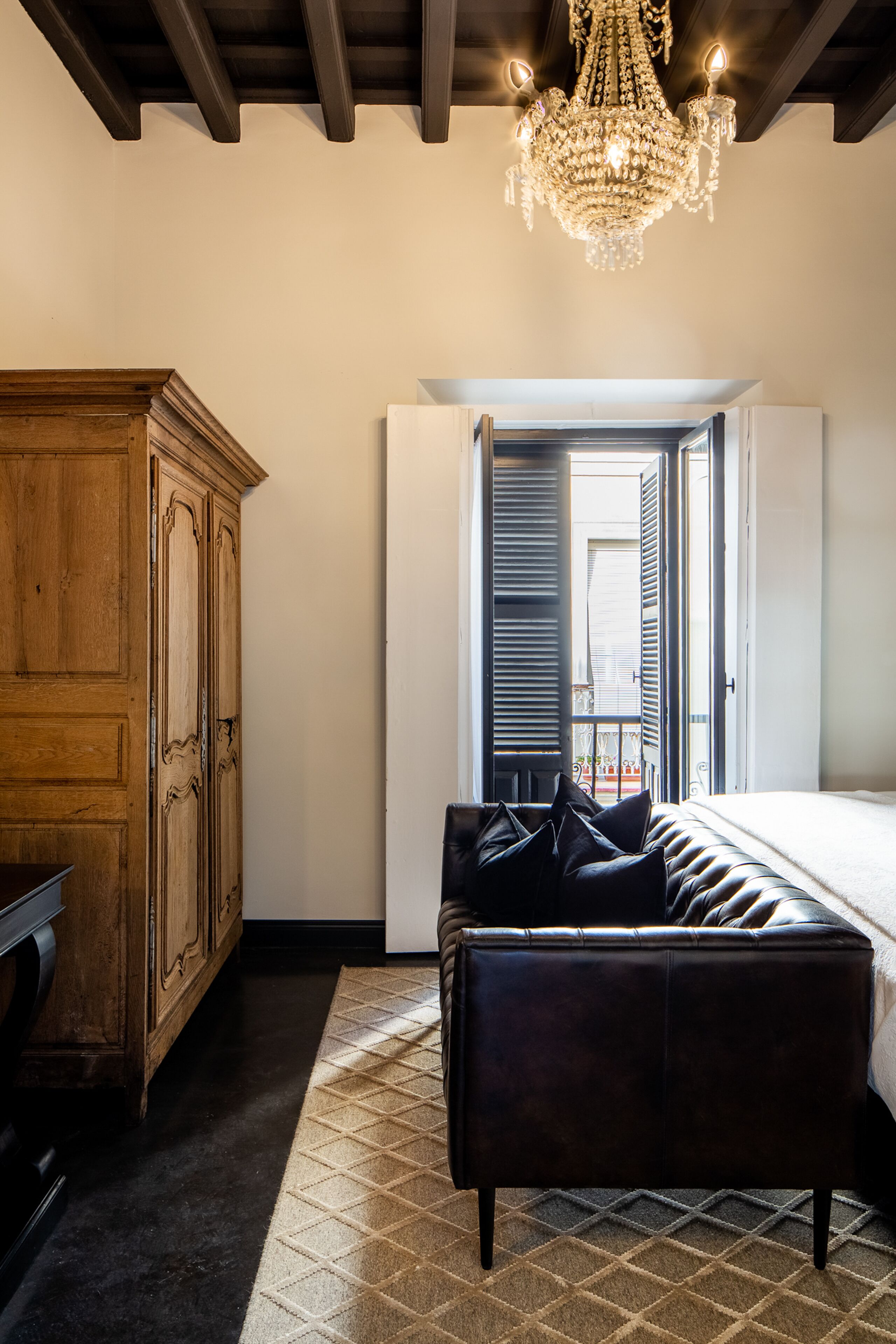 Une chambre avec une armoire en bois, un canapé en cuir, un lustre et une fenêtre avec des volets.