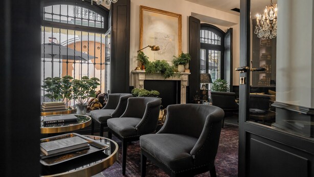 A luxurious lounge area with dark leather armchairs, a fireplace, and a large window with a view of a building.