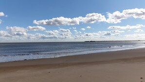 Ein Strand mit einer Pier, die sich ins Wasser erstreckt, sandigem Ufer und Fußabdrücken im Sand.