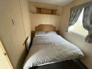 Een kleine slaapkamer met een enkel bed, een inbouwkast boven het bed en een raam met gordijnen.