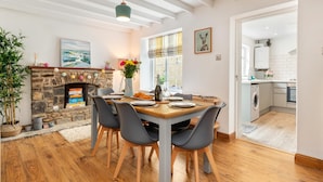 A dining area with a stone fireplace, wooden flooring, and a view into the kitchen. - Ivydene - Beautiful Cottage Stone Throw From Beach Wonderful Sea Views (Saundersfoot)