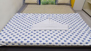 Un lit bien fait, recouvert d’une courtepointe à motifs floraux bleus et agrémenté d’une serviette blanche.