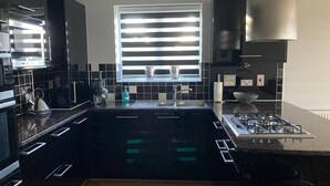 A modern kitchen with black cabinetry, a window with blinds, a gas stove, and a built-in oven. - Beautiful Sea view apartment in Carlyon Bay (Carlyon Bay)