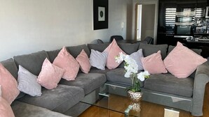 A modern living room with a sectional sofa, a glass coffee table, and a kitchen in the background. - Beautiful Sea view apartment in Carlyon Bay (Carlyon Bay)