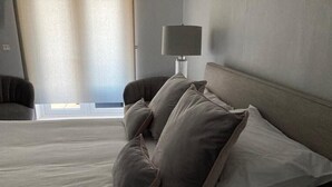 A hotel room with a bed, pillows, a lamp, and a window with curtains. - Beautiful Sea view apartment in Carlyon Bay (Carlyon Bay)