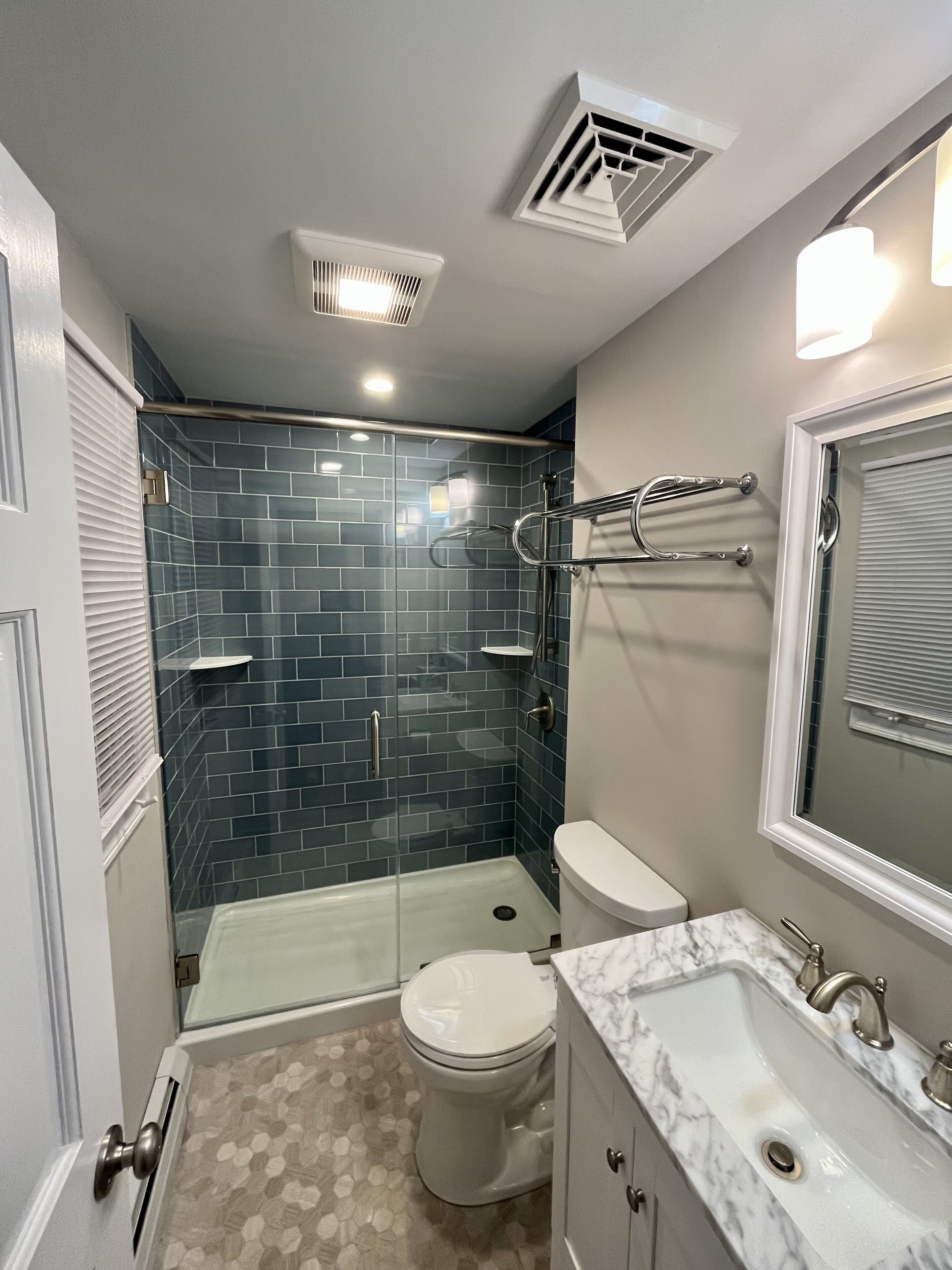 Une salle de bain compacte dotée d’une douche à parois de verre, de toilettes et d’un lavabo avec un plan de travail en marbre.