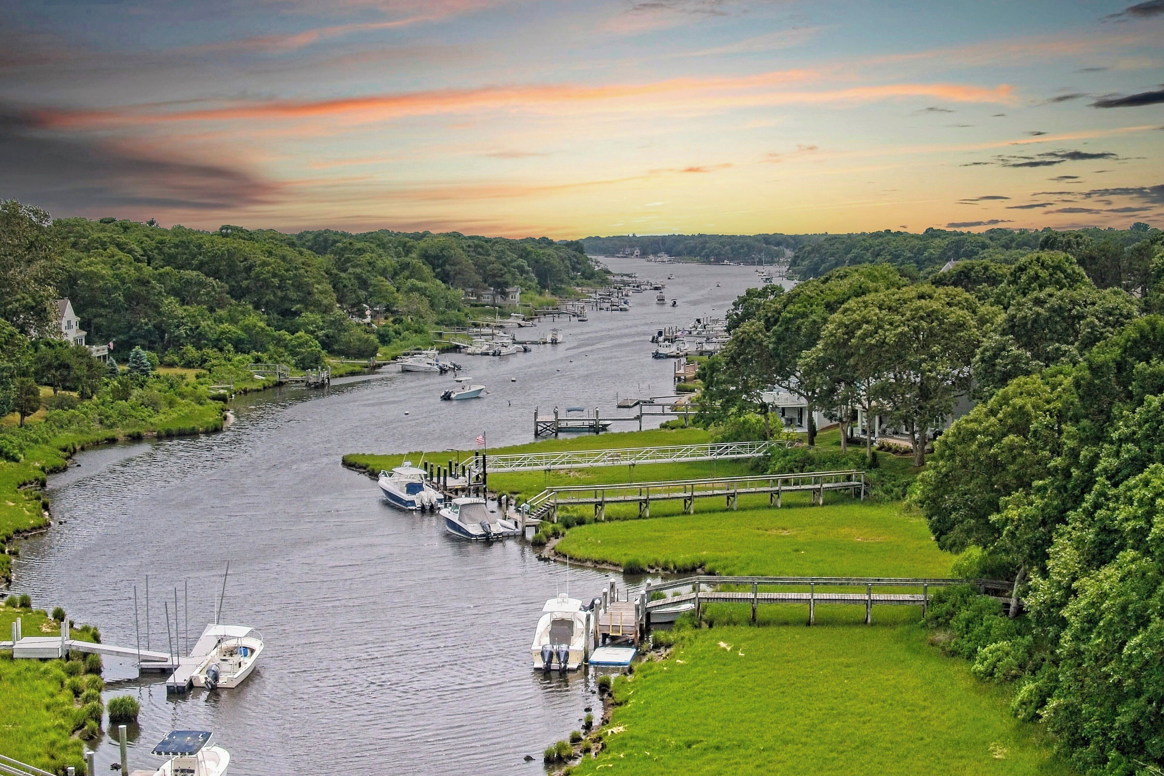 A river with boats docked along the banks, surrounded by lush greenery and a bridge connecting the two sides.