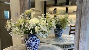 A dining area with a round table, two blue and white vases with white flowers, and a wooden chair. - Stunning Interior designed cottage (Chipping Campden)