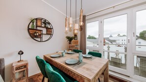 Comedor con mesa de madera, sillas tapizadas de verde e iluminación colgante.