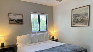 A neatly made bed with white bedding and a gray blanket, two bedside lamps, a window with blinds, and two framed pictures on the walls. - Cozy Oro Valley Retreat, close to Golf, Trails & Fine Dining-Dog Friendly (Tucson)