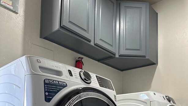 A front-loading washer and dryer in a laundry room with gray cabinets above. - Cozy Oro Valley Retreat, close to Golf, Trails & Fine Dining-Dog Friendly (Tucson)