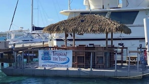 Een boot met een bord voor Tropical Tiki Tours, een rieten parasol en houten ligstoelen.