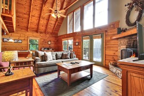 A cozy log cabin interior with a fireplace, wooden furniture, and large windows. - Grandma's Gift: Beautiful mountain views and great privacy! (Gatlinburg)