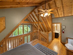 Een houten interieur met een schuine kap, een bed, een badkamer en uitzicht op groen buiten.