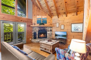 A cozy cabin interior with a stone fireplace, a television, and a comfortable seating area.