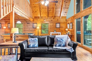 A cozy cabin interior with a black leather sofa, wooden walls, and a pool table.