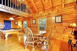 Ein Holzblockhaus-Interieur mit Billardtisch, Esstisch und Stühlen.