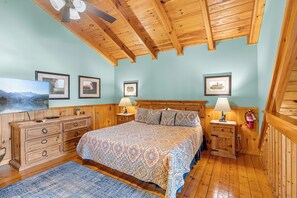 A bedroom with a wooden ceiling, a bed with patterned bedding, a dresser, and framed pictures on the wall. - Honeysuckle- A perfect 1 bedroom cabin to retreat to! (Gatlinburg)