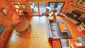 A cabin interior with a wooden floor, a fireplace, a ceiling fan, and a dining area with a table and chairs.