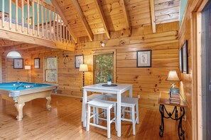 A wooden interior with a pool table, a dining area, and a staircase.
