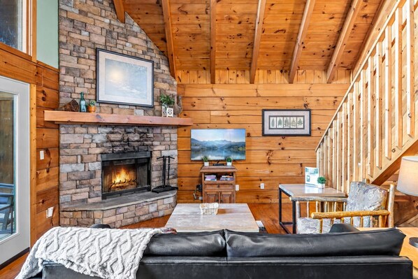 A cozy cabin interior with a stone fireplace, wooden walls, a television, and a sofa.