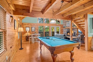 Un interior de madera con mesa de billar, zona de estar y chimenea.