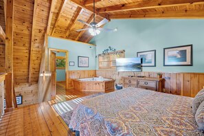 A wooden cabin interior with a large bed, a bathroom with a bathtub, and a ceiling fan.