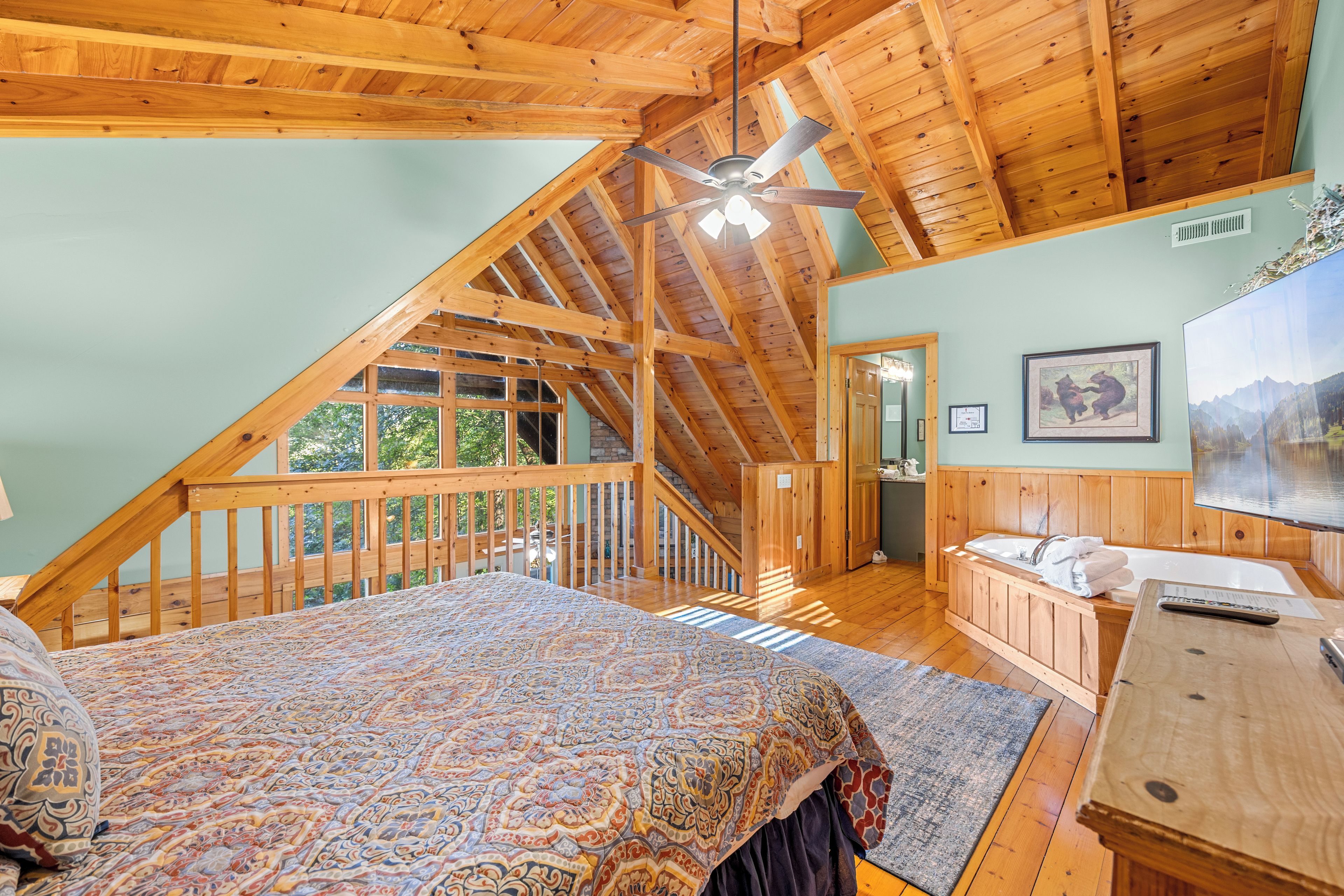 Une chambre avec un grand lit, un plafond en bois, un ventilateur de plafond, une salle de bain avec une baignoire et un escalier menant à un étage supérieur.