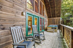 A wooden deck with two rocking chairs, a hot tub, and a glass door leading to an interior space. - Honeysuckle- A perfect 1 bedroom cabin to retreat to! (Gatlinburg)
