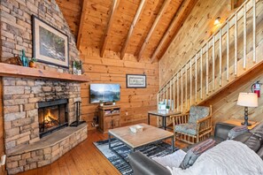 A cozy log cabin interior with a fireplace, wooden walls, a television, and a comfortable seating area. - Honeysuckle- A perfect 1 bedroom cabin to retreat to! (Gatlinburg)