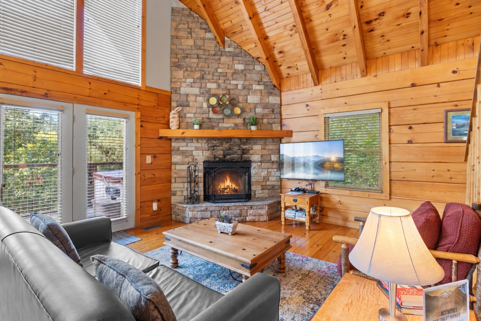 A cozy cabin interior with a stone fireplace, wooden walls, a television, and comfortable seating.