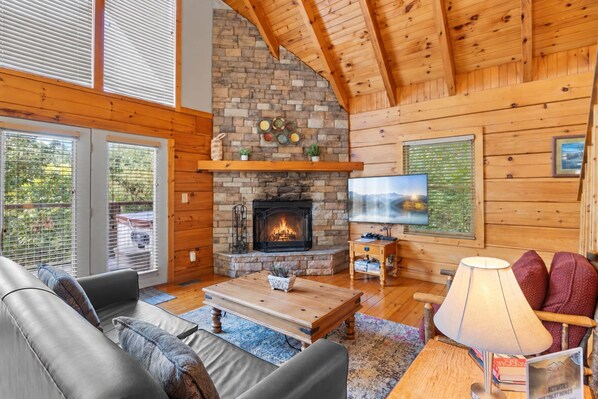 Un intérieur de chalet chaleureux avec une cheminée en pierre, des murs en bois, un téléviseur et des sièges confortables.
