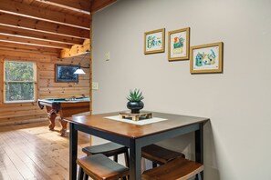 A wooden room with a pool table, a billiards cue, and framed artwork on the wall.