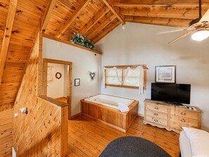 Ein Holzinnenraum mit Holzbalkendecke, einer Badewanne, einem Fernseher und einer Kommode.