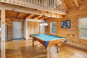 A wooden interior with a pool table, a door, and a window with blinds.