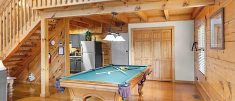 A wooden interior with a pool table, a staircase, and a kitchen area.