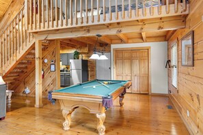 A wooden interior with a pool table, a staircase, and a kitchen area.