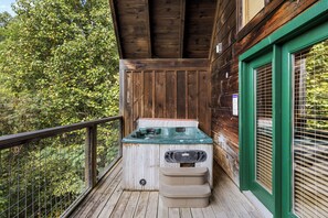A wooden deck with a hot tub, surrounded by a wooden wall and a green door.