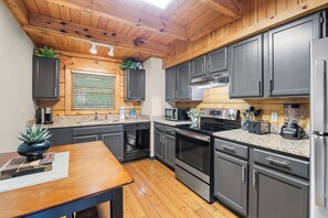 Une cuisine moderne avec des meubles de couleur sombre, des appareils électroménagers en acier inoxydable et un plancher en bois.