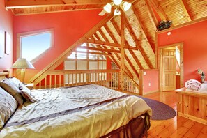 A bedroom with a sloped ceiling, a large bed, a wooden desk, and a window.