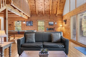 A wooden interior with a pool table, a sofa with cushions, a coffee table with a plant, and a billiards table.