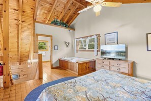 A wooden cabin interior with a large bed, a television, and a bathtub.